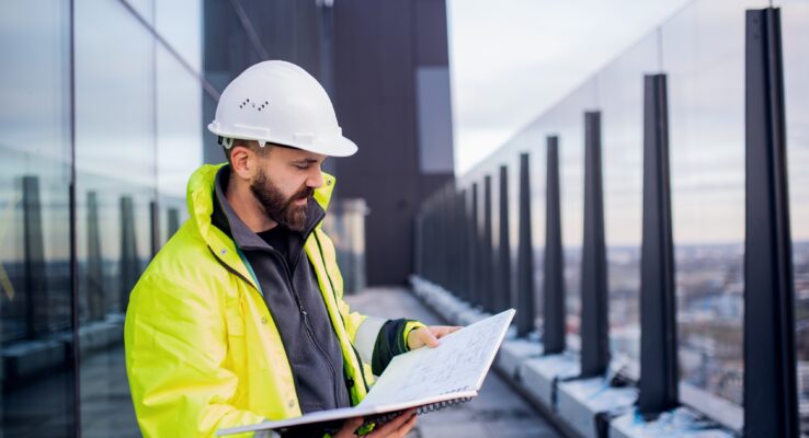 Man engineer standing on construction site, holding blueprints.