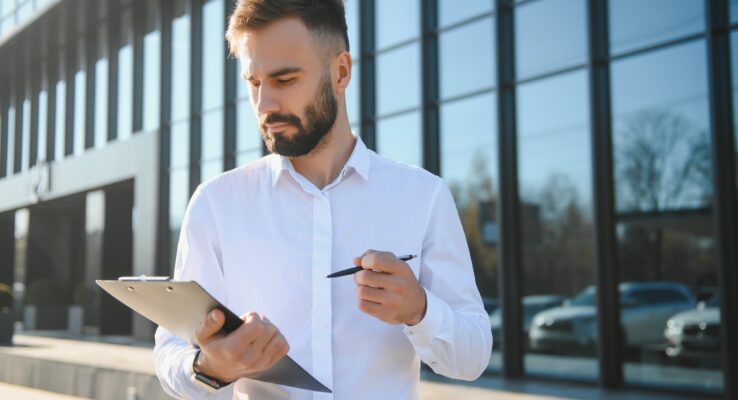 Male Realtor Standing Outside Residential Property Holding Keys