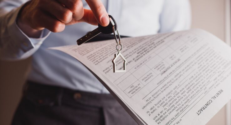 Manager offers keys to house holding contract in other hand. Rental and buying a property